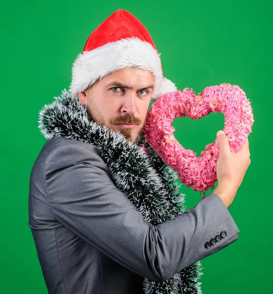 Man in love happy wear santa hat celebrate christmas green background. Merry christmas and happy new year. Hipster hold heart symbol of love. Bring love to family holiday. Spread love around