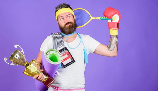 Sport shop assortment. Man bearded athlete hold sport equipment jump rope fitness mat boxing glove expander racket and golden goblet. Choose favorite sport. Sport concept. On way to achievement