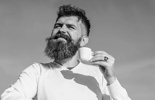 Homem com barba longa desfrutar de café. Homem com barba e bigode no rosto sorridente bebe café, fundo azul do céu, desfocado. Homem barbudo com caneca de café, bebe café. Conceito de provador de café — Fotografia de Stock