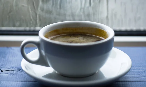 Fresh brewed coffee in white cup or mug on windowsill. Coffee time on rainy day. Wet glass window and cup of hot coffee. Autumn cloudy weather better with caffeine drink. Enjoying coffee on rainy day