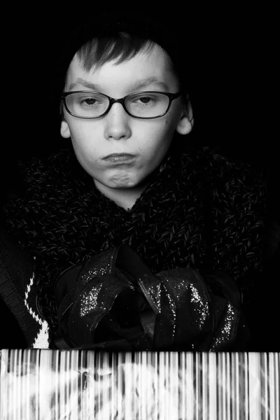 Pequeno menino sério ou garoto nerd bonito em óculos, chapéu e cachecol de malha na moda no fundo preto mantém caixa de presente colorido com bo vermelho — Fotografia de Stock