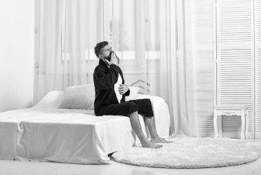 Uyanış kavramı. Yatak, beyaz perde arka plan üzerinde elbise içinde adam oturur. Maço sakal ve bıyık halsiz kalkarak ve sabah esneme ile. Adam sabah esneme uykulu yüz