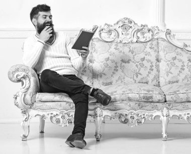 Sakal ve bıyık oturur barok tarzı kanepe, tutar kitap, beyaz duvar arka plan üzerinde olan adam. Adam zevk ile eski kitap okuma. Mizahi edebiyat kavramı. Maço yüz kitap okuma gülüyor üzerinde