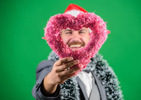 Man in love happy wear santa hat celebrate christmas green background. Spread love around. Merry christmas and happy new year. Hipster hold heart symbol of love. Bring love to family holiday