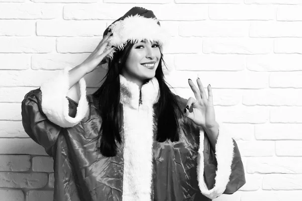 Гарненька сексуальна дівчина Санта або усміхнена брюнетка в червоному светрі з різдвяним або різдвяним капелюхом і показує добре на білій цегляній стіні — стокове фото