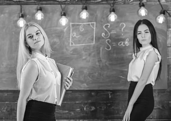 Señoras listas para empezar una clase privada, pizarra de fondo. Profesores en ropa formal con libro y gafas de aspecto atractivo. Concepto de lección privada. Profesores atractivos con exceso de trabajo después de las clases — Foto de Stock