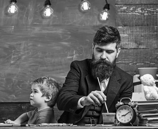 Teacher with beard, father drawing while little son hang out near, in classroom, chalkboard on background. Arts lesson concept. Child and teacher on busy face painting, drawing — Stock Photo, Image