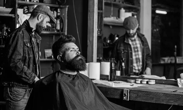 Hipster client getting haircut. Man with beard covered with black cape waiting while barber changing clipper grade. Client with beard ready for trimming or grooming. Haircut process concept — Stock Photo, Image