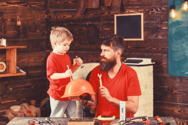 Güvenlik ve koruma kavramı. Baba, anne-baba sakal ile oğlu Emanet okul atölye öğretim kask tutar. Evlat, çocuk neşeli cıvata veya vida, baba ile handcrafting sırasında eğlenmek tutar