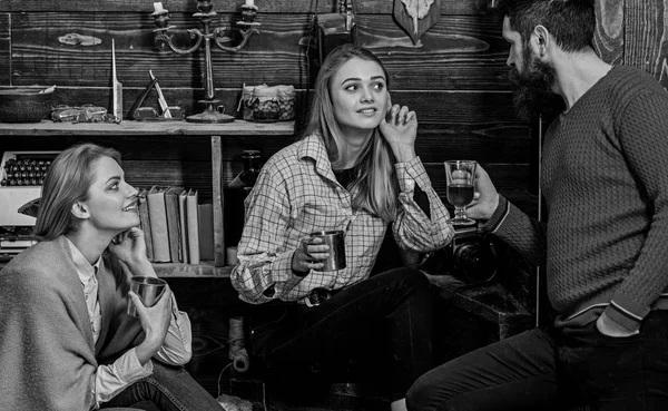 Familia disfrutar de la conversación en la casa de guardabosques. Concepto de conversación sincera. Chicas y hombres en caras felices sostienen tazas metálicas, hablando. Amigos, familia pasar agradable noche, fondo interior — Foto de Stock