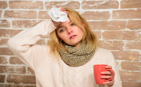 Woman feels badly ill sneezing. Girl in scarf hold tea mug and tissue. Runny nose and other symptoms of cold. Cold and flu remedies. Remedies should help beat cold fast. Tips how to get rid of cold