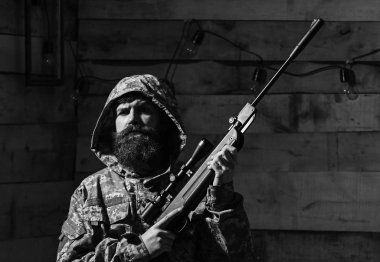 Sakallı adam başlıklı kamuflaj elbiseler, ahşap iç arka plan giyer. Maço gamekeepers evinde sıkı yüzünde. Hunter, silahla acımasız hipster tüfek avcılık için hazırlayın. Avcı kavramı