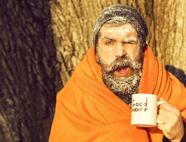 Donmuş adam göz kırpıyor, sakal ve bıyık sakallı hippi beyaz kış günü açık havada doğal adam Kupası'nda ısınma içkiyle turuncu battaniyeye sarılmış frost ile kaplı — Stok fotoğraf