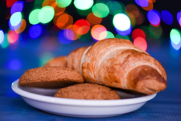 Croissant and oat cookies on white plate. Winter holiday tradition. Sweets for Santa Claus and his helpers. Santa treats recipe. Treats for Santa concept. What do kids around world leave for Santa