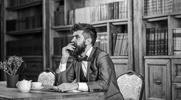 Old style and male fashion. Bearded man sits in library with old book. Mature man in smart suit thinks. Professor with thoughtful face. Education, self-study, liberal arts, thoughts, dreams concept