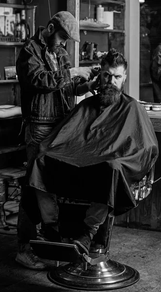 Hipster lifestyle concept. Hipster client getting haircut. Barber with clipper trimming hair on temple of client. Barber with hair clipper works on hairstyle for bearded man barbershop background — Stock Photo, Image