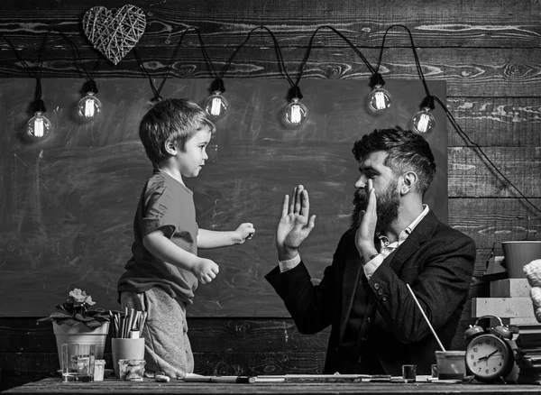 Art lesson concept. Child cheerful and teacher have fun during drawing. Talented artist spend time with son. Teacher with beard, father teaches son to draw in classroom, chalkboard on background