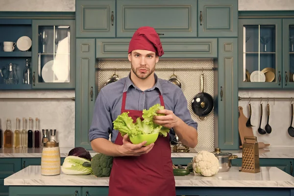 Man chef in red hat, apron hold green salad leaves