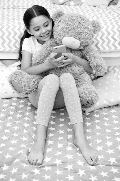 Send message sweet dreams. Girl child sit on bed with teddy bear in her bedroom. Kid prepare to go to bed. Girl kid long hair cute pajamas relax plush teddy bear toy. Child smartphone send message