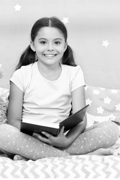 Okuma fairytale önce yatağına git. Kız çocuk kitap okumak bir oyuncak ayı ile yatağa otur. Çocuk yatmaya hazırlanın. Keyifli zaman rahat yatak odasında. Kız çocuk uzun saçlı şirin pijama rahatla ve oyuncak ayı için kitap okumak — Stok fotoğraf