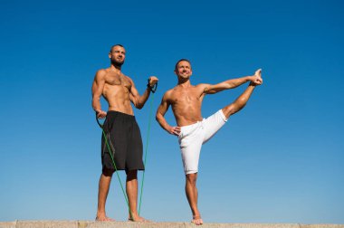 Muscular men training on fresh air. Reach balance by virtue of yoga. Sport and health care. Daily exercises to maintain health. Health and yoga practice. Towards health. Men practice yoga outdoors clipart