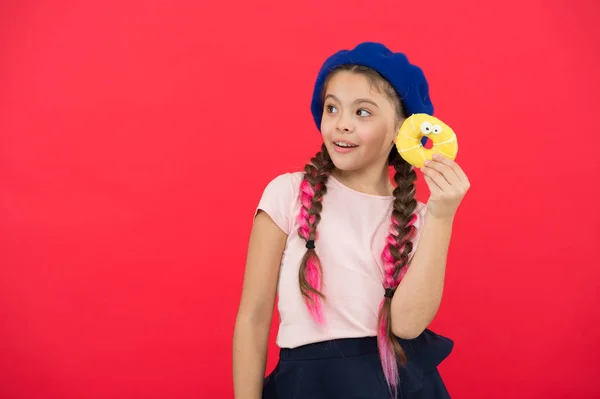 Kind spielerisches Mädchen bereit, Donut zu essen. Süßwarengeschäft und Bäckereikonzept. Kinder große Fans von gebackenen Donuts. unmöglich, frisch zubereiteten Donut widerstehen. Mädchen halten glasierten niedlichen Donut in der Hand roten Hintergrund — Stockfoto