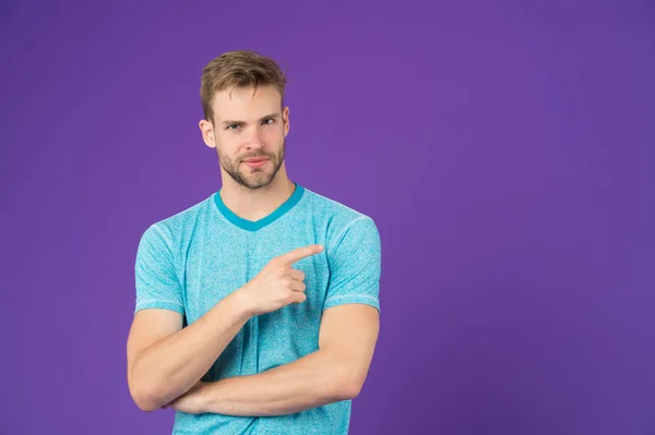 Look here. Man muscular handsome unshaven guy on violet background pointing finger copy space. Masculinity concept. Man with strong muscular arms. Does having muscular body make you more confident
