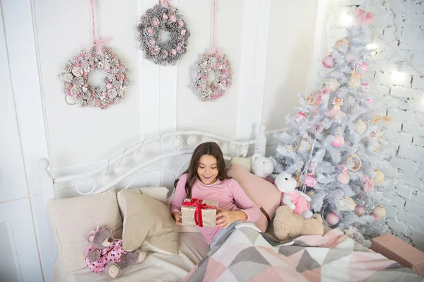 Dziecko czeka Boże Narodzenie w sypialni. Dzieciak leżał w łóżku relaks. Dom jest najlepszym miejscem na świecie. Dziewczyna małe dziecko, relaks na łóżku światła wnętrza z ozdobami świątecznymi. Koncepcja Wigilia Bożego Narodzenia — Zdjęcie stockowe