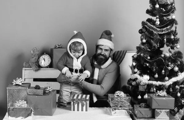 Santa and little assistant among gift boxes near Christmas tree. — Stock Photo, Image