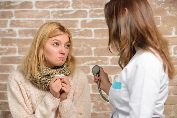 Woman feels badly ill sneezing. Girl in scarf hold tissue while doctor examine her. Cold and flu remedies. Recognize symptoms of cold. Remedies should help beat cold fast. Tips how to get rid of cold