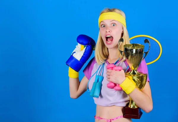 Sport for every day. Sport shop assortment. Girl successful modern woman hold golden goblet of sport champion and equipment blue background. How to find time for everything. Sport equipment store