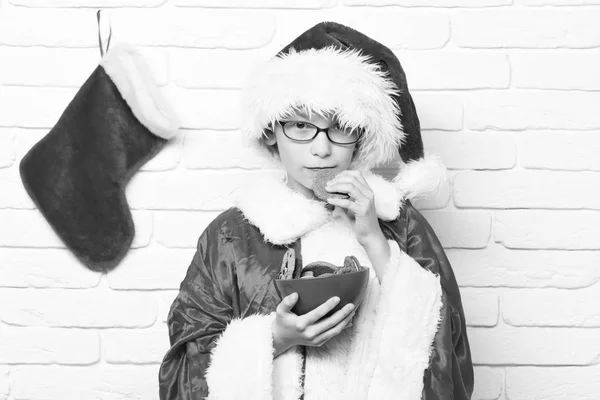 Dekoratif Noel veya Noel çorap veya çikolata kalça kurabiye kase beyaz tuğla duvar arka planda tutan önyükleme ile kırmızı kazak ve yeni yıl şapkalı gözlüklü Genç Sevimli Noel Baba Çocuk — Stok fotoğraf