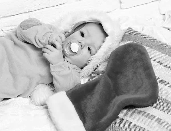 Niño pequeño con adorable cara curiosa en suéter amarillo con maniquí en sombrero de año nuevo y navidad o medias de Navidad o bota sobre fondo de pared de ladrillo blanco — Foto de Stock