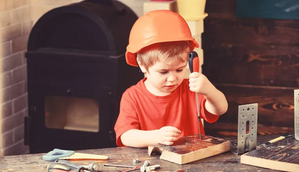 Мальчик играет как строитель или ремонтник, работает с инструментами. Мальчик в оранжевой каске или шлеме, задний план учебной комнаты. Ребенок мечтает о будущей карьере в архитектуре или строительстве. Концепция детства — стоковое фото