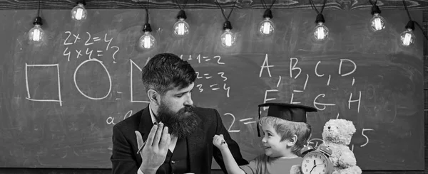 Padre enseña matemáticas hijo. Profesora de vestimenta formal y alumna de mortero en aula, pizarra de fondo. Chico alegre estudiando con el profesor. Concepto de lección aritmética —  Fotos de Stock