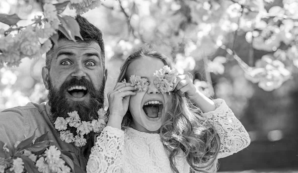 Father and daughter on happy face play with flowers as glasses, sakura background. Child and man with tender pink flowers in beard. Girl with dad near sakura flowers on spring day. Family time concep — Stock Photo, Image