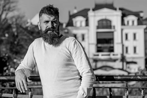 Man with long beard enjoy view from balcony. Relaxation concept. Bearded man have rest on sunny day outdoors. Man with beard and mustache on calm face at balcony, urban background, defocused
