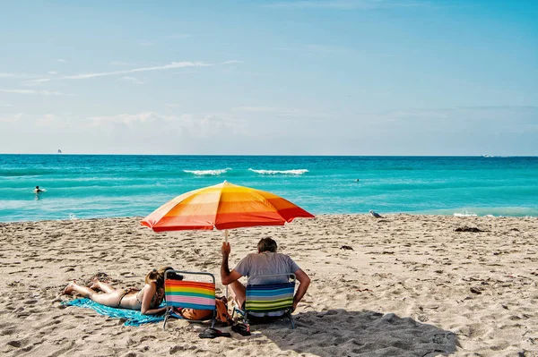 Padre e hija relajándose bajo paraguas naranja en la playa de arena — Foto de Stock