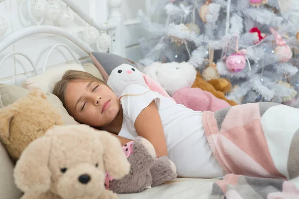 Enjoying xmas at home. Little child sleep at Christmas tree. Little girl lying in bed with toys. Cute girl fell asleep on Christmas night. Sleeping child. Peaceful sleep and rest on winter holidays — Stock Photo, Image