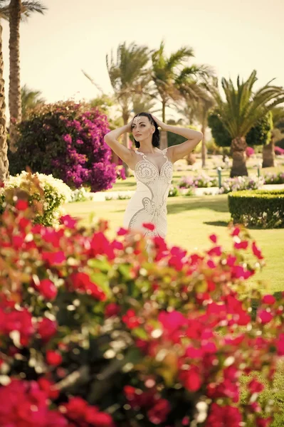 Çiçek açması çiçekli kadın poz. Bahçede esmer saçlı manken. Güzellik kız makyaj ve çekici bir görünüm ile. Yaz gününde beyaz elbiseli seksi gelin. Düğün ve Bayan günü kutlama