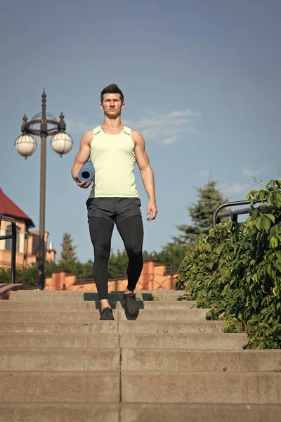 Mannen idrottsman i träningsoverall med gym yogamatta kommer trappa ner — Stockfoto