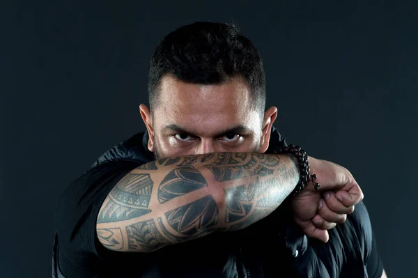 Tattooed elbow hide male face. Tattoo culture concept. Man brutal unshaven hispanic appearance tattooed arm. Bearded man posing with tattoos. Brutal macho with tattoos. Masculinity and brutality
