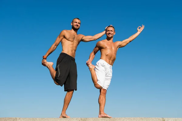 Vers la santé. Les hommes pratiquent le yoga à l'extérieur. Des hommes musclés s'entraînent à l'air frais. Atteindre l'équilibre en vertu du yoga. Sport et soins de santé. Exercices quotidiens pour maintenir la santé. Santé et pratique du yoga — Photo