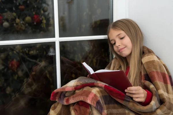 즐거운 휴가 위한 동화입니다. 리틀 리더 창틀에 격자 무늬 앉아에 싸여 있다. 어린 소녀는 크리스마스 이야기를 읽고 즐길 수 있습니다. 작은 아이 크리스마스 이브에 책을 읽었다. 어린이 책. 매직 크리스마스 정신 — 스톡 사진
