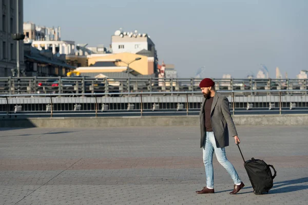 Ajustar vivir en una ciudad nueva. Lleva una bolsa de viaje. Hombre barbudo viaje hipster con bolsa de equipaje sobre ruedas. Viajero con maleta llegar aeropuerto estación de tren de fondo urbano. Hipster listo disfrutar de viajes — Foto de Stock