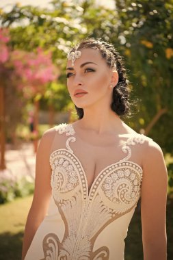 Esmer saç takı diadem kadınla. Şehvetli kadın beyaz düğün elbise ile inci boncuklar. Gelin Makyaj yüz. Glamour görünüm ve makyaj güzellik kız. Yaz bahçesinde bir modeldir