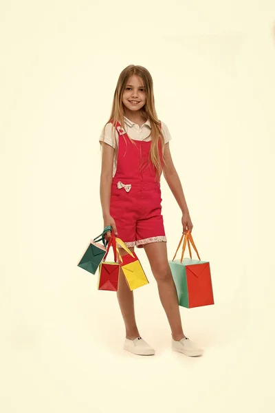 A bevásárló szatyrok elszigetelt fehér kislánya. Gyermek mosolya a papír táskák. Boldog gyerek vásárló a divat színû munkaruhában. Ünnepek előkészítése és ünneplés. Miután a bevásárló nap. eladó és fekete péntek — Stock Fotó