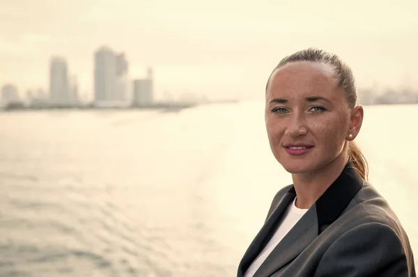 Business woman with freckled face in jacket posing at sea