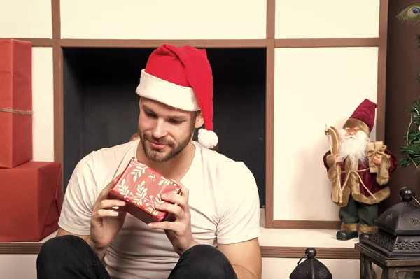 Man in santa hat look at red box at fireplace — Stock Photo, Image