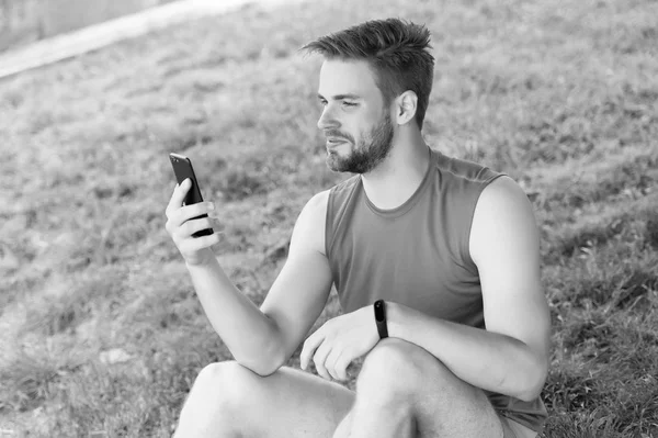 Sport gadget concept. Athlete with fitness tracker or pedometer. Man athlete on busy face setting up fitness tracker with smartphone app, nature background. Sportsman training with pedometer gadget
